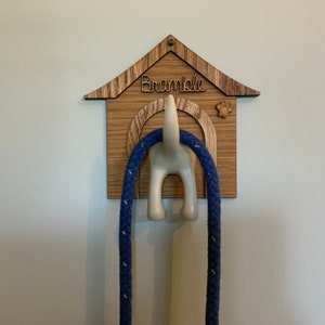 May include: Wooden dog house shaped leash holder with the name "Bramble" engraved on the front. A blue leash is hanging from the hook shaped like a dog's rear end.