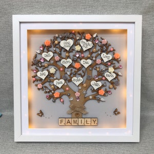 May include: A light-up wooden family tree with names written on hearts and flowers. The tree is decorated with pink, white, and peach flowers, pearls, and glitter. The words "FAMILY." are spelled out in wooden blocks at the bottom of the tree.