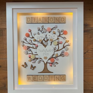 May include: A white framed illuminated picture with a wooden tree design. The tree has pink and white flowers, rhinestones, and butterflies. The words "DIAMOND", "WEDDING", "Mum", "Dad", and "7th September 1963" are spelled out with wooden tiles.