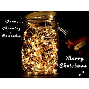May include: A glass jar filled with warm, glowing fairy lights. The jar is sealed with a lid and has a metal clasp. Text on the image reads "Warm, Charming & Romantic" and "Merry Christmas". A hand holds a tag that says "MxSaver".