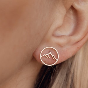 Puede incluir: Un par de pendientes de oro con un diseño de cordillera dentro de un círculo.