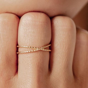 Op de afbeelding: Een gouden ring met een gedraaid ontwerp. De ring wordt gedragen aan de vinger van een persoon.