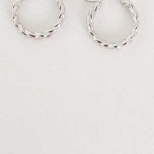 May include: A pair of silver hoop earrings with a twisted design.