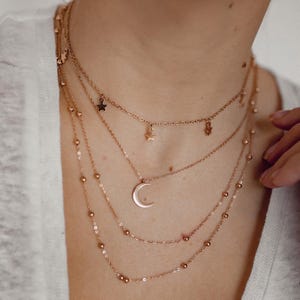 May include: A layered necklace set with a crescent moon pendant and star charms. The necklace is made of gold-toned metal.