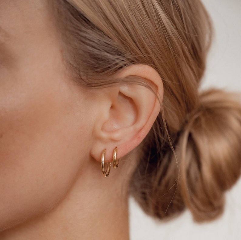 May include: A pair of gold hoop earrings, one larger than the other, worn in the ear of a person with blonde hair.