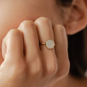 K&ouml;nnte beinhalten: Ein goldener Ring mit einem wei&szlig;en runden Stein in der Mitte.