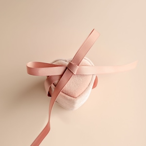 Könnte beinhalten: Eine rosafarbene, herzförmige Samtbox mit einem rosa Satinband, das darum gebunden ist.