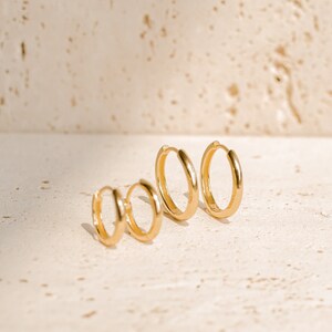 May include: Three gold hoop earrings of different sizes. The earrings are arranged in a row from largest to smallest.