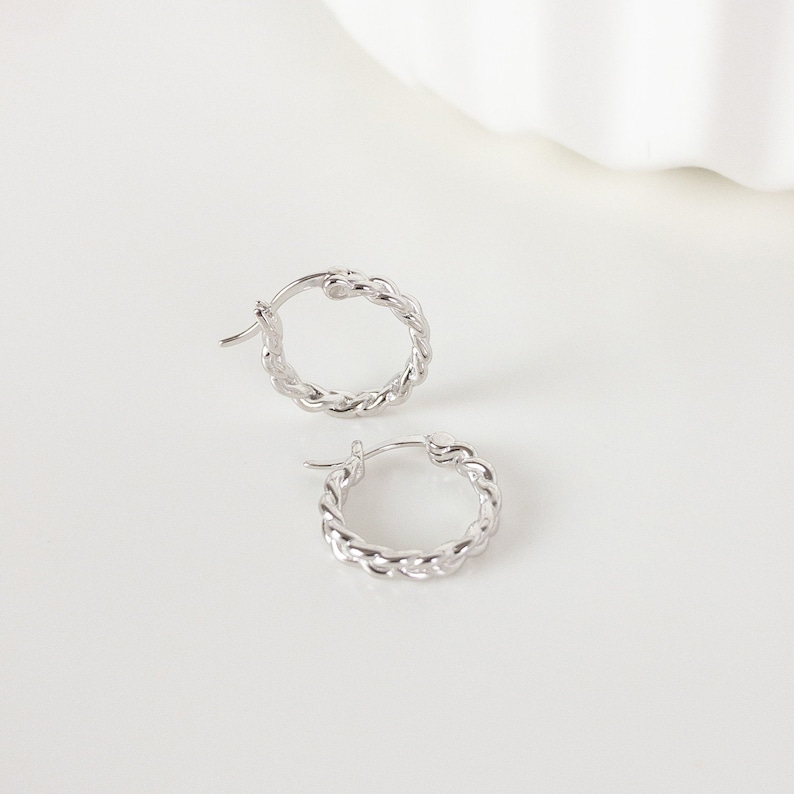 May include: A pair of silver hoop earrings with a twisted rope design.