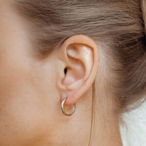 May include: A close-up of a person's ear with a silver hoop earring. The earring is simple and elegant, with a smooth, polished finish.