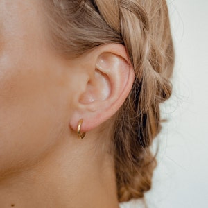 May include: A close-up of a person's ear with a small gold hoop earring.