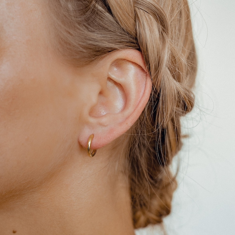 May include: A close-up of a person's ear with a small gold hoop earring.
