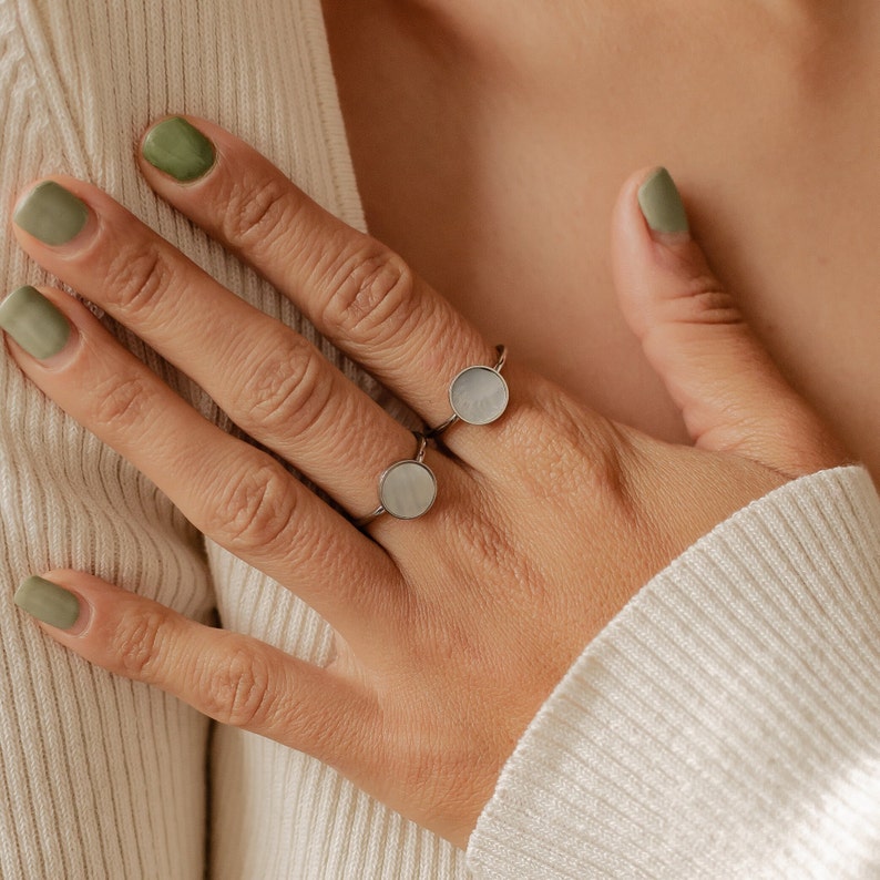K&ouml;nnte beinhalten: Zwei silberne Ringe mit wei&szlig;en, opalartigen Steinen. Die Ringe werden am Zeigefinger einer Hand getragen.