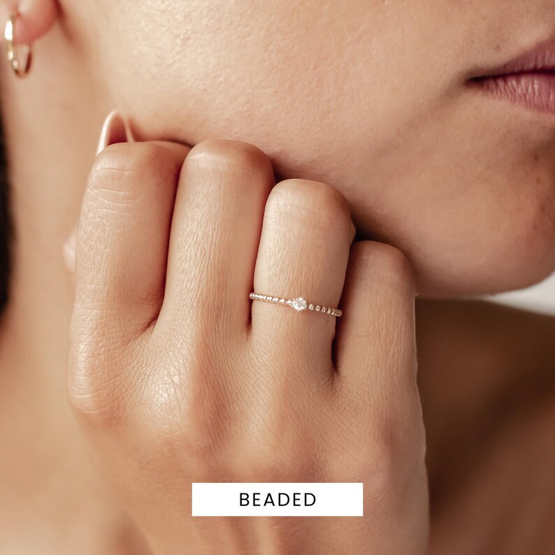 K&ouml;nnte beinhalten: Ein zarter Goldring mit einem kleinen Diamanten in der Mitte. Der Ring ist mit winzigen goldenen Kugeln besetzt.