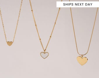 May include: Three gold-colored necklaces with heart pendants. The necklaces have different chain styles, including a delicate chain with a small heart, a beaded chain with a white heart pendant, and a snake chain with a solid heart pendant. The text "SHIPS NEXT DAY" is visible.