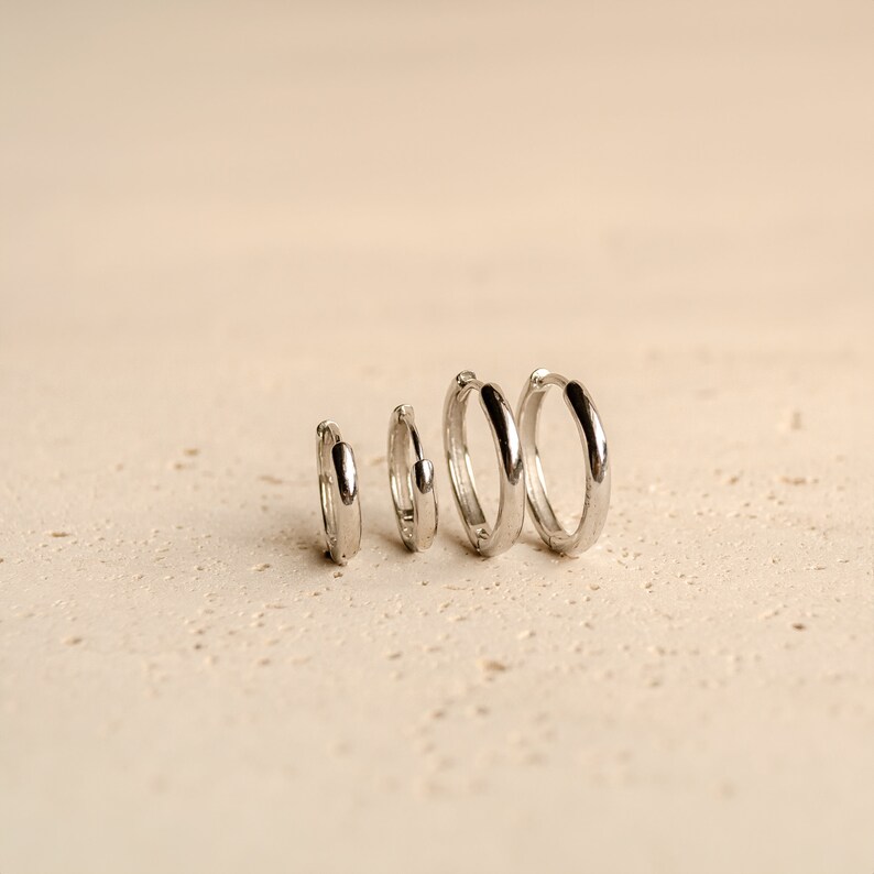May include: Four silver hoop earrings of different sizes, arranged in order of size from smallest to largest.