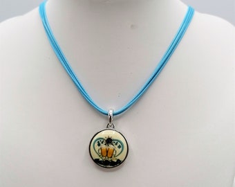 Peut inclure: Un collier avec un pendentif rond et un cordon bleu clair. Le pendentif a un fond crème avec un motif de deux chopes de bière et un cœur bleu. Le pendentif mesure environ 2,5 cm de diamètre.