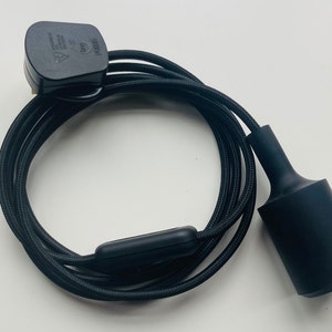 Op de afbeelding: Zwarte hanglamp met een zwart gevlochten snoer, een zwarte stekker en een inline aan/uit-schakelaar. De lamp heeft een cilindrische kap en is ontworpen voor gebruik binnenshuis.