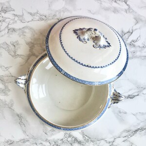 May include: A white porcelain serving bowl with a blue and gold trim. The bowl has two handles and a matching lid with a decorative knob.