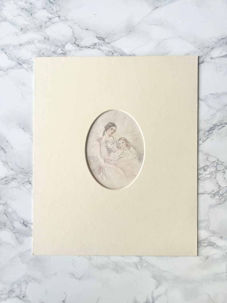 May include: An oval print of a mother and child, set within a cream-coloured mount. The print is a delicate etching, depicting the figures in soft lines. The mount is rectangular, with a marble-patterned background.