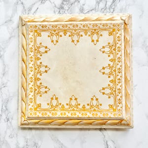 Può includere: Un vassoio quadrato in ceramica caratterizzato da un centro color crema con un motivo decorativo a bordo giallo dorato. I bordi rialzati del vassoio sono scolpiti con una trama a corda, rifiniti in una combinazione di colori giallo dorato e crema.
