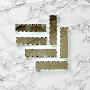 Peut inclure: Un ensemble de six carreaux rectangulaires en miroir biseauté avec un bord ondulé. Les carreaux sont disposés en quinconce sur une surface en marbre blanc.