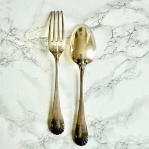 Peut inclure: Ensemble de couverts en argent comprenant une fourchette et une cuillère. La fourchette a quatre dents, et la cuillère a un bol arrondi. Les deux ustensiles présentent des détails décoratifs sur les manches.