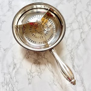 Peut inclure: Un plat de service argenté doté d'un bol rond perforé divisé en trois sections par un séparateur central en métal. Le plat présente un bord perlé et une poignée lisse et allongée, reflétant une finition métallique polie sur l'ensemble.