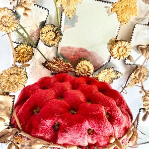 May include: A red, tufted cushion with a decorative gold-coloured base. The cushion is surrounded by gold-coloured floral and leaf accents, and small, square mirrors. The overall design is ornate and vintage-inspired.