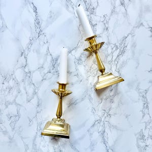 Peut inclure: Deux bougeoirs en or avec des bougies blanches sur une surface en marbre blanc.