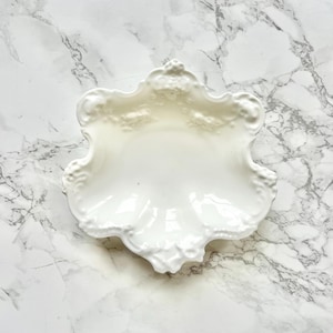 Peut inclure: Un plat en porcelaine blanche avec un bord festonné et un motif floral complexe. Le plat est parfait pour servir de petites friandises ou pour ranger des bijoux.