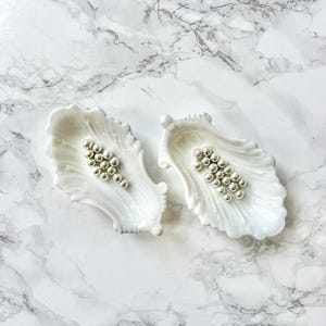 Puede incluir: Dos platos de cerámica blanca con forma de concha con cuentas plateadas en su interior.