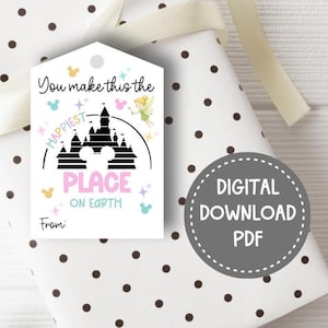 Puede incluir: Una etiqueta de regalo con el texto "You make this the happiest place on earth" con una silueta de castillo y un hada. La etiqueta está en un regalo envuelto con lunares y una cinta.