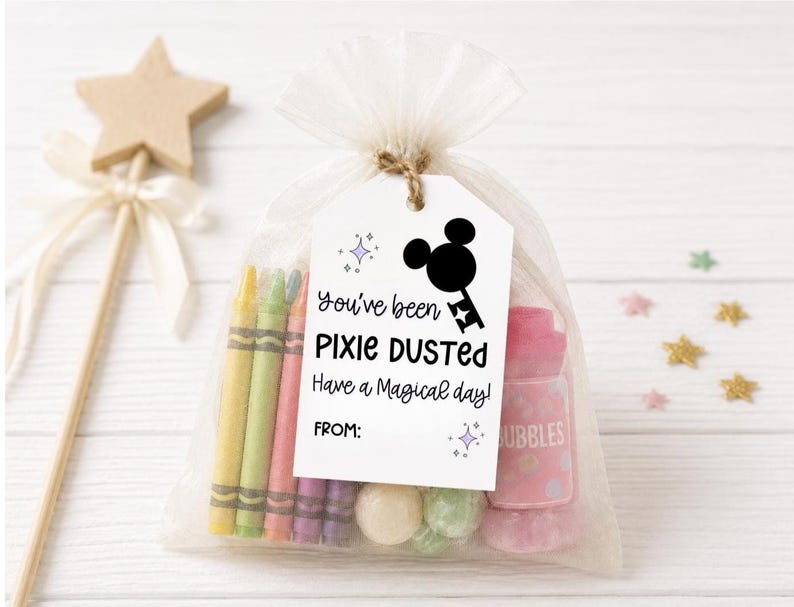 May include: A sheer white organza drawstring bag containing colorful crayons, small round candies, and a pink bubble bottle. A white rectangular tag attached with twine features a black silhouette of a key with mouse ears and the text You've been PIXIE DUSTED Have a Magical day! FROM: