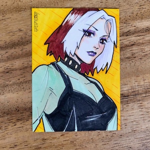 May include: Illustration of a comic book character with white and burgundy hair, wearing a black top and choker. The artwork is on a rectangular card with a yellow and orange background. The artist's signature is in the upper left corner.