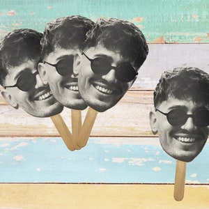 May include: Four black and white photo booth props of a person wearing sunglasses and smiling. The props are attached to wooden sticks.