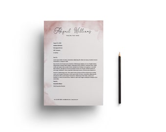 May include: A letterhead with the name "Abigail Williams" in elegant script, featuring a watercolor-style pink and brown wash. A black pencil rests beside the letter. The text "TAGLINE TEXT HERE" is below the name.