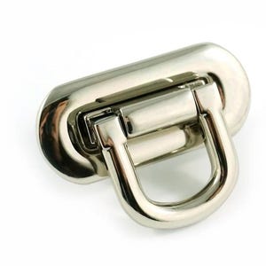May include: A shiny, silver-colored purse clasp with a rectangular base and a curved, D-shaped handle. The metal hardware is designed for bags and accessories, providing a secure closure.
