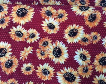 May include: Close-up of a fabric with a repeating sunflower pattern. The sunflowers have yellow and orange petals with dark brown centers. The background is a deep red with small, evenly spaced dots.
