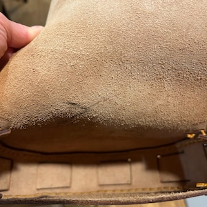 May include: The inside of a brown leather bag with a suede lining. The bag has multiple compartments and is lined with a brown fabric.