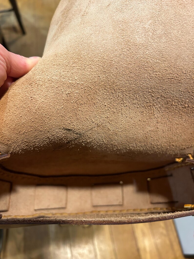 May include: The inside of a brown leather bag with a suede lining. The bag has multiple compartments and is lined with a brown fabric.