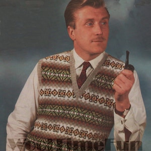 Op de afbeelding: Een beige gebreide vest met een geometrisch patroon in bruin, groen en oranje. Het vest heeft een V-hals en wordt gedragen over een wit shirt met een rode das.