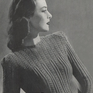 May include: A black and white photograph of a woman wearing a knitted jumper with a cable knit pattern. The jumper has a round neckline and long sleeves. The woman is looking to the right and has her hair styled in a wave.