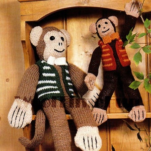 May include: Two knitted monkey toys wearing vests. The monkey on the left is brown with a green and white striped vest and a white bow tie. The monkey on the right is brown with an orange and brown striped vest and a brown bow tie.