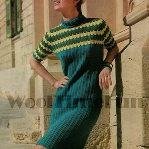 Può includere: Una donna indossa un abito di maglia a righe verdi e gialle con un cappello giallo e occhiali da sole blu. È in piedi accanto a un muro di pietra.