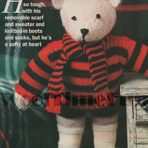 May include: A knitted teddy bear wearing a red and black striped sweater and a black and white scarf. The bear is holding a red, yellow, and green ball. The text "Footballer teddy" is printed below the bear.