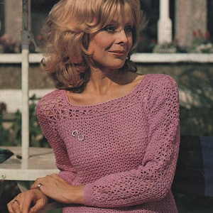 May include: A light purple crochet sweater with long sleeves and a square neckline. The sweater features an openwork design and a small brooch. The text "FOUR PLY to fit 86 to 97 cm bust" is visible. A vintage garment, perfect for a retro look. The sweater is a handmade item.