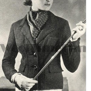 May include: A woman wearing a black tweed jacket with a white polka dot scarf. She is holding a long, thin stick in her right hand.