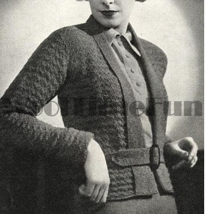 May include: A black and white photo of a woman wearing a knitted cardigan with a belt. The cardigan has a textured pattern and a V-neck.