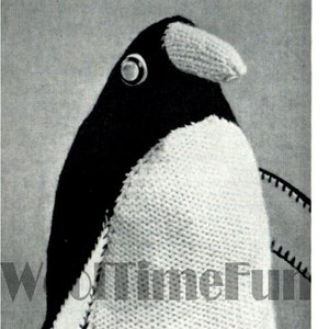 Può includere: Un giocattolo di pinguino di maglia nera e bianca. Il pinguino ha la testa e le ali nere, il corpo bianco e un piccolo becco arancione. Il pinguino è in piedi su una superficie grigia.